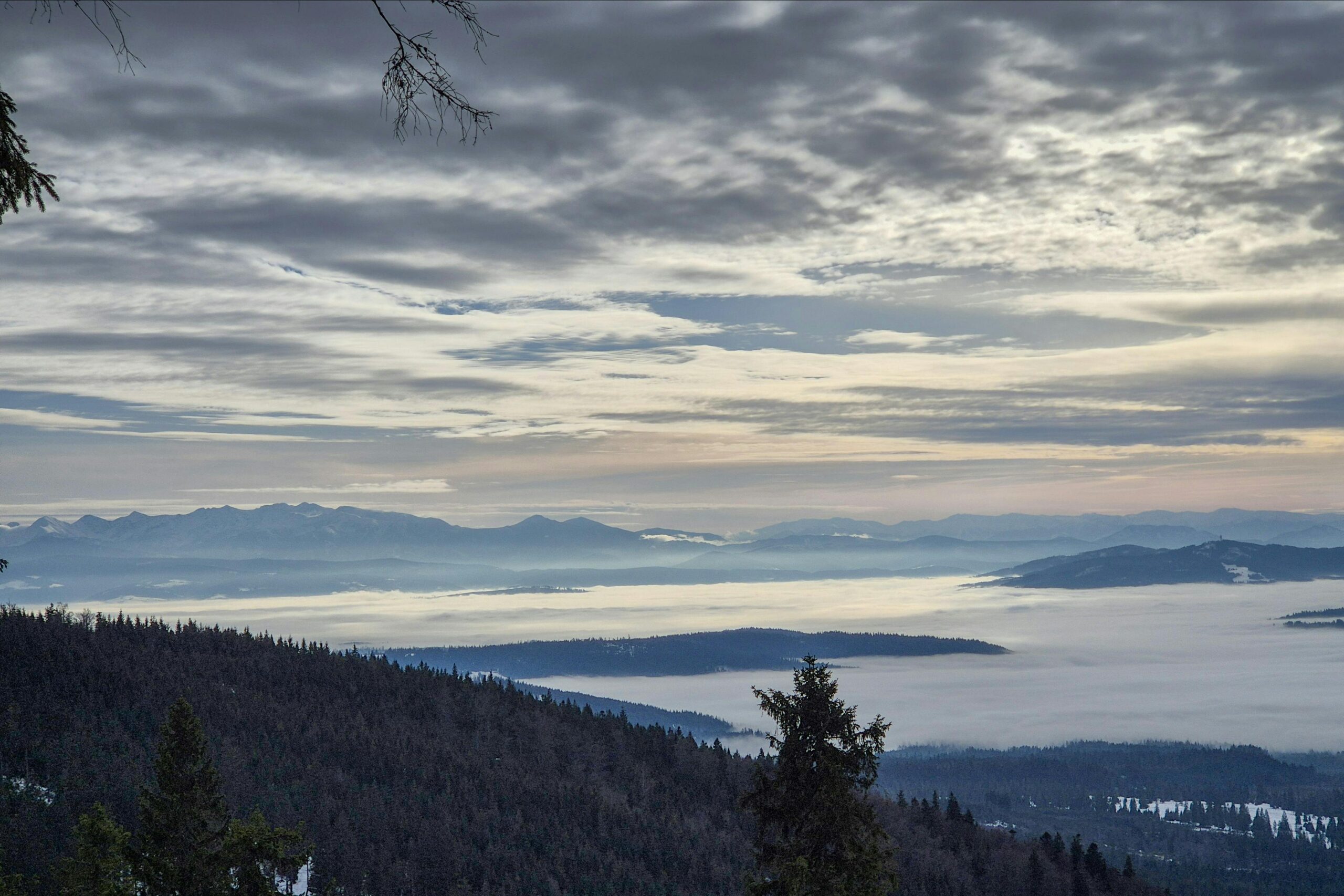Serene winter view of mist-covered valleys and mountain range in Poland, under dramatic skies.