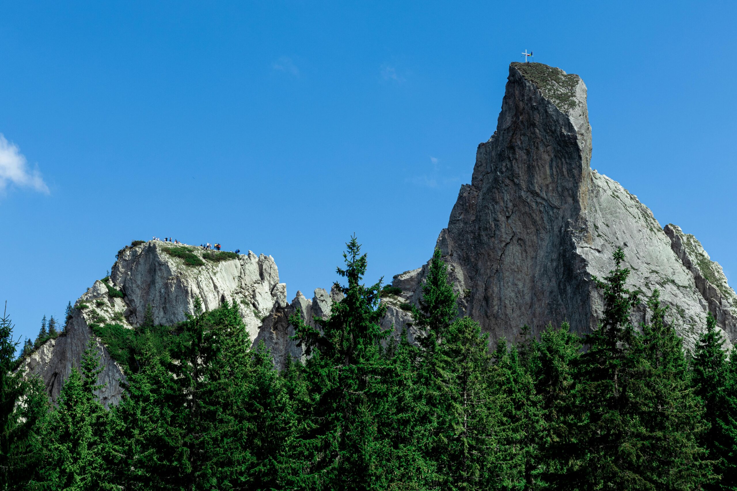 Majestic rock formations of Ceahlău Massif surrounded by evergreen forests under a clear blue sky.